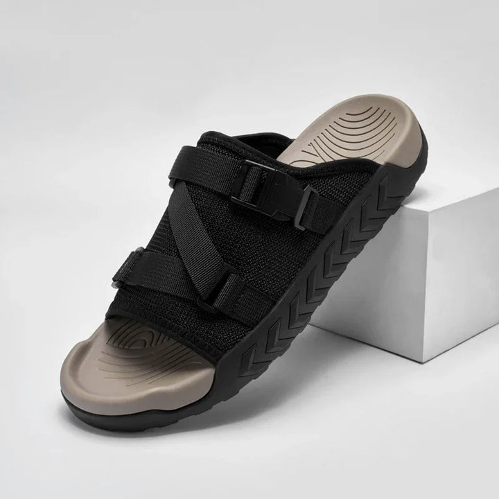 black slide sandal with adjustable straps and textured sole resting on white block
