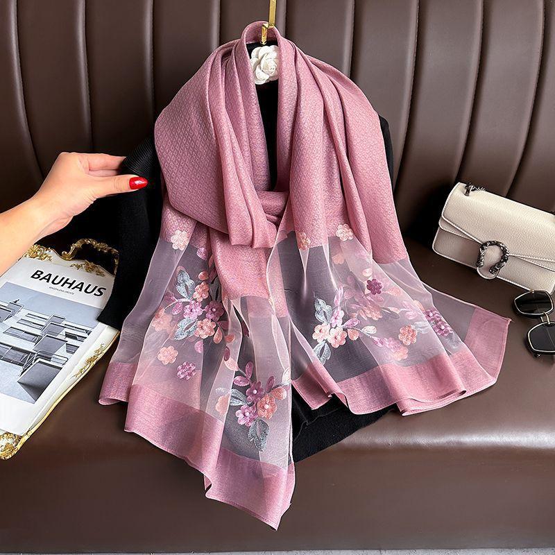 Elegant pink floral embroidered chiffon scarf draped over black garment on brown leather sofa