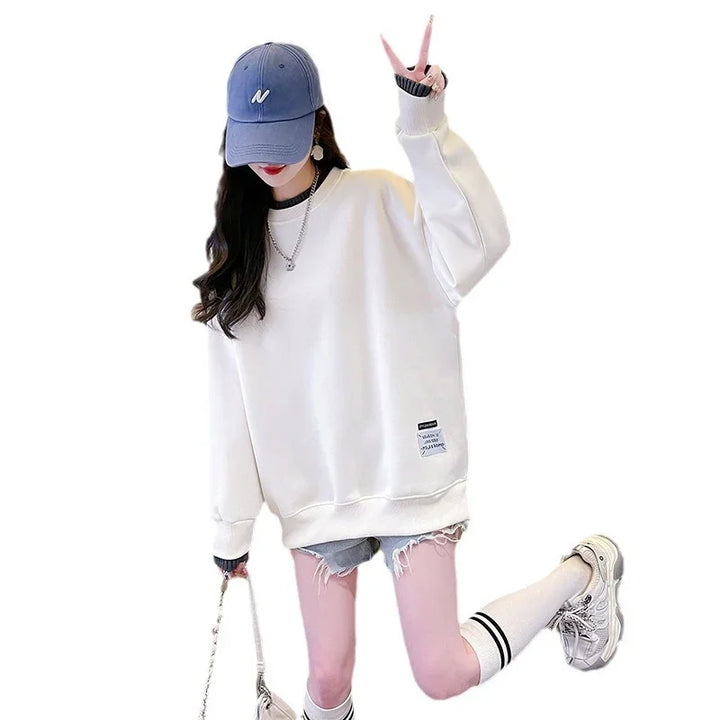 Young woman in white oversized sweatshirt, ripped denim shorts, blue cap, white knee socks, and white sneakers posing with peace sign