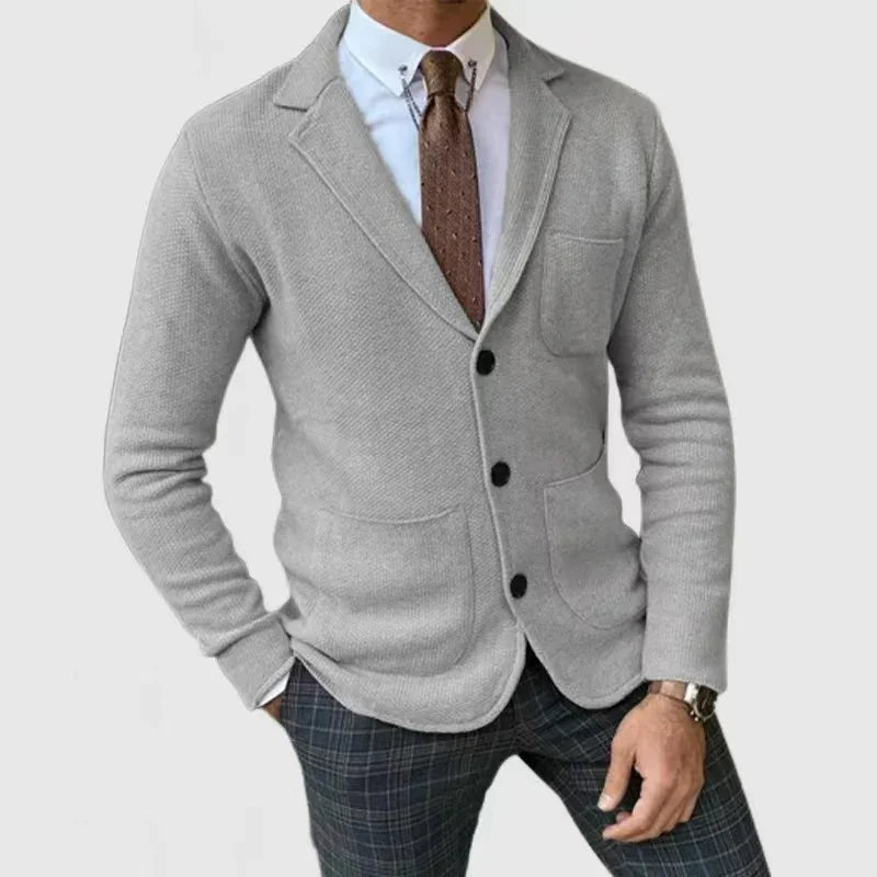 Man wearing gray knit blazer with black buttons, white shirt, brown tie, and plaid pants