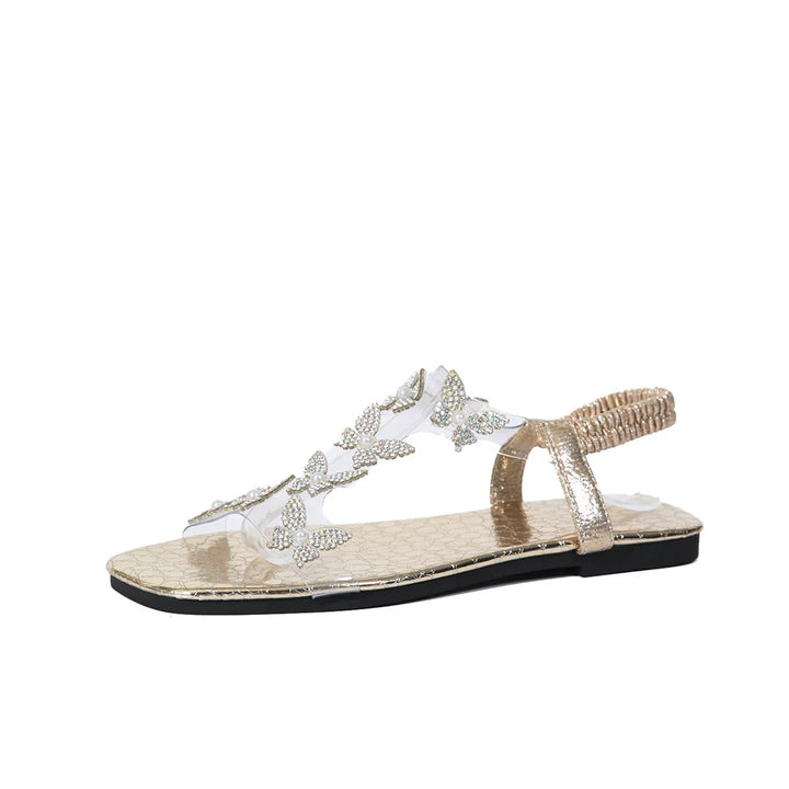 Gold flat sandal with clear strap adorned with rhinestone butterfly and pearl decorations