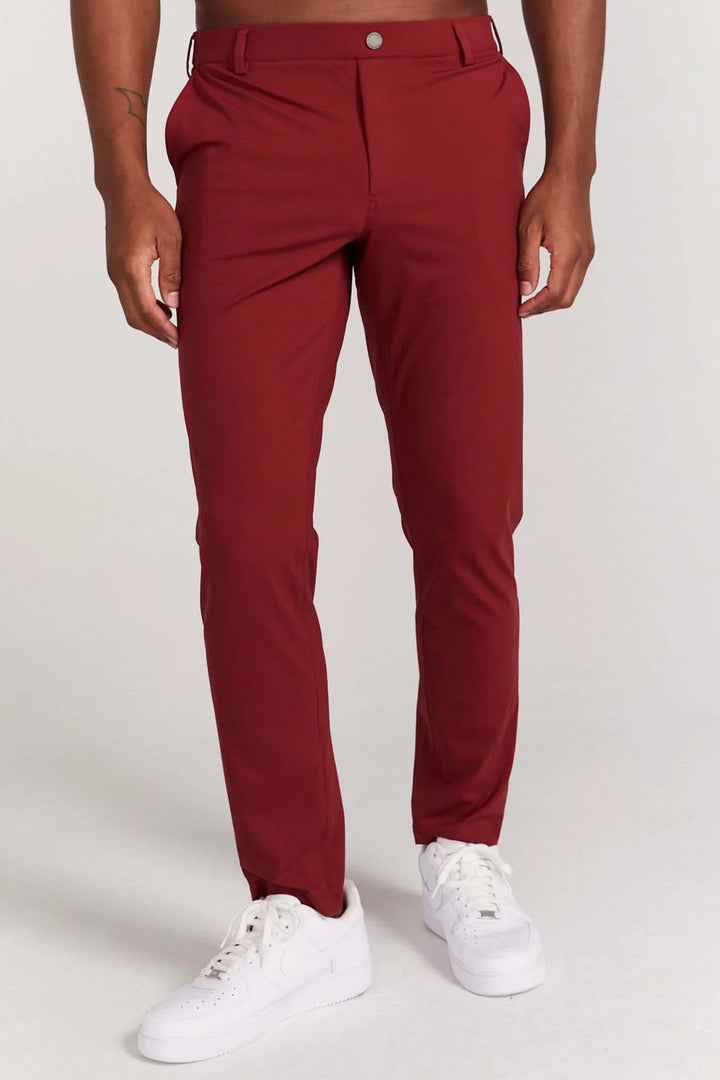 Male model wearing slim fit burgundy pants with white sneakers on a plain background