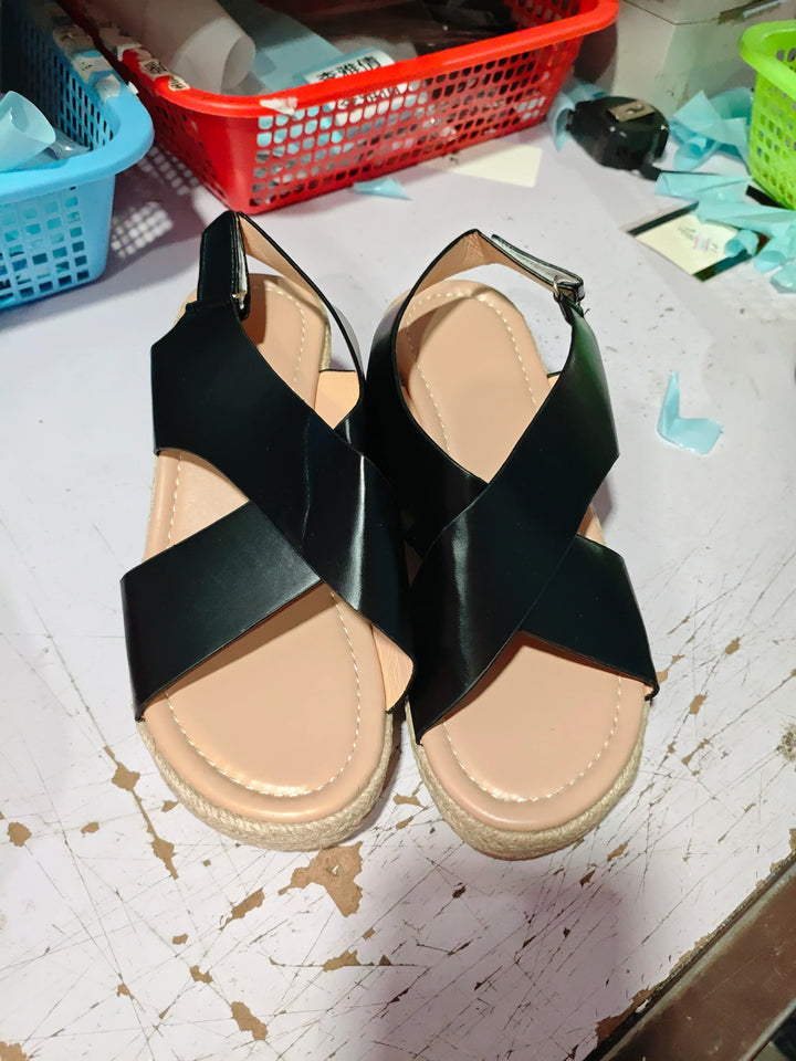 Pair of black crisscross strap sandals with beige cushioned soles on a worn white surface