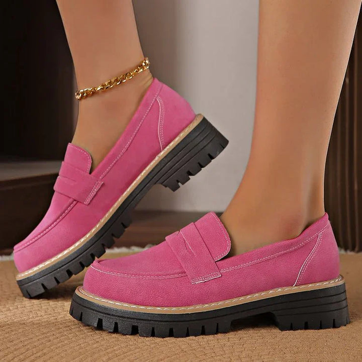 Close-up of feet wearing pink suede loafers with chunky black lug soles and a gold anklet