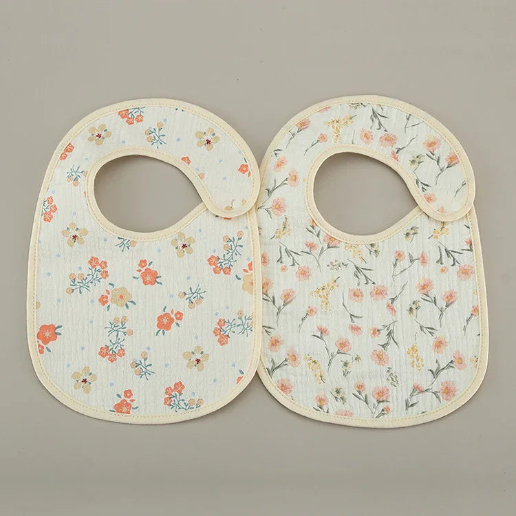 Two floral pattern baby bibs with curved neck closures on a neutral background
