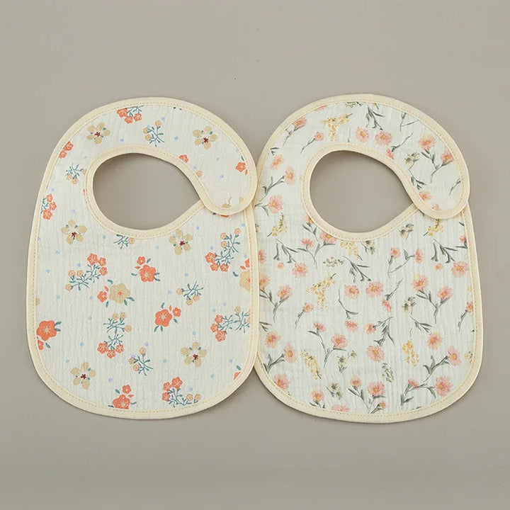 Two floral pattern baby bibs with curved neck closures on a neutral background