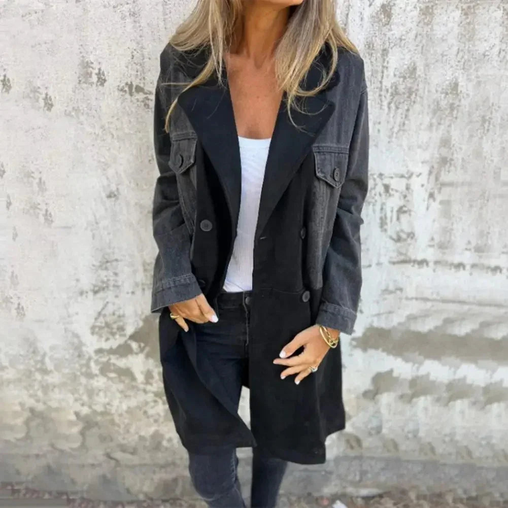 Woman wearing black and grey color-block trench coat with white top and black jeans against textured wall