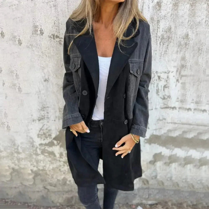 Woman wearing black and grey color-block trench coat with white top and black jeans against textured wall