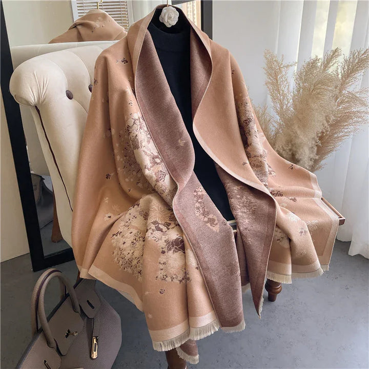 Beige floral patterned shawl draped on cream armchair with black turtleneck and grey handbag nearby