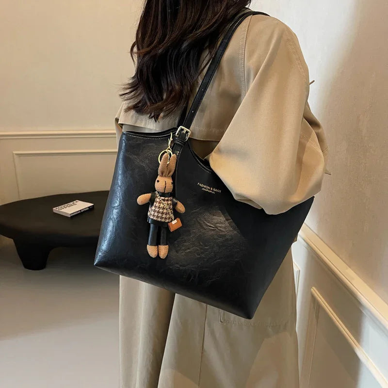 Black leather shoulder handbag with cute bunny keychain worn by woman in beige trench coat indoors