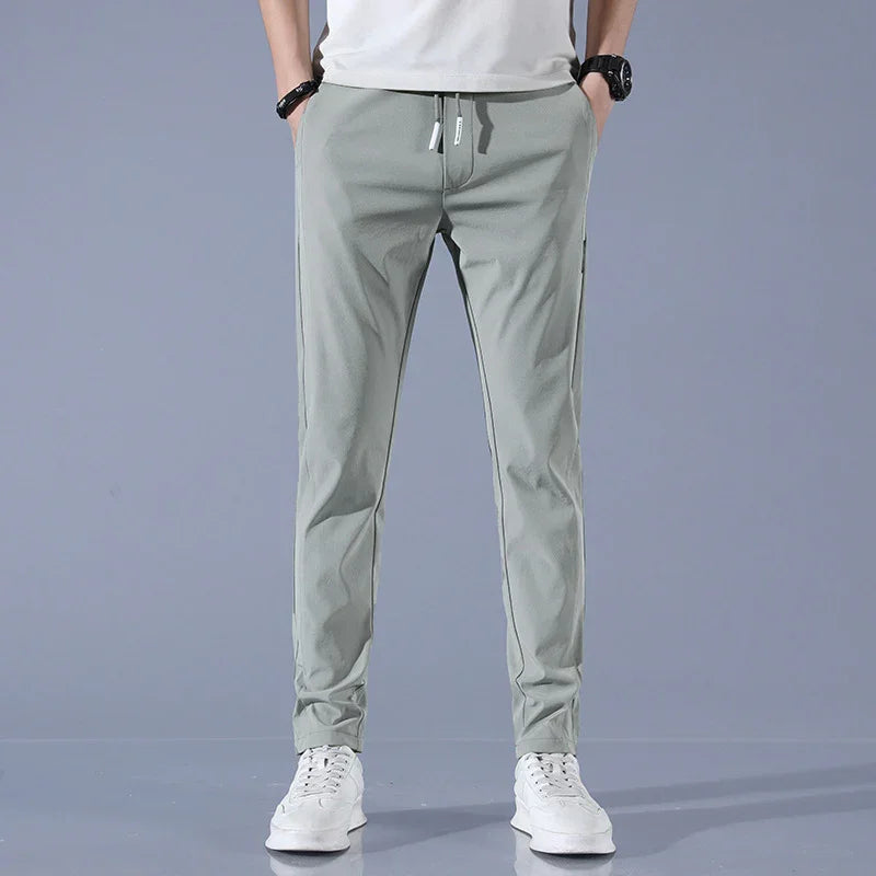 Men's light gray casual jogger pants with drawstring waist and white sneakers on gray background