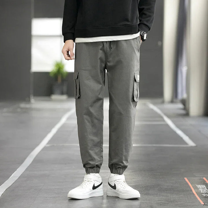 Man wearing gray cargo jogger pants and white Nike sneakers in an urban indoor setting