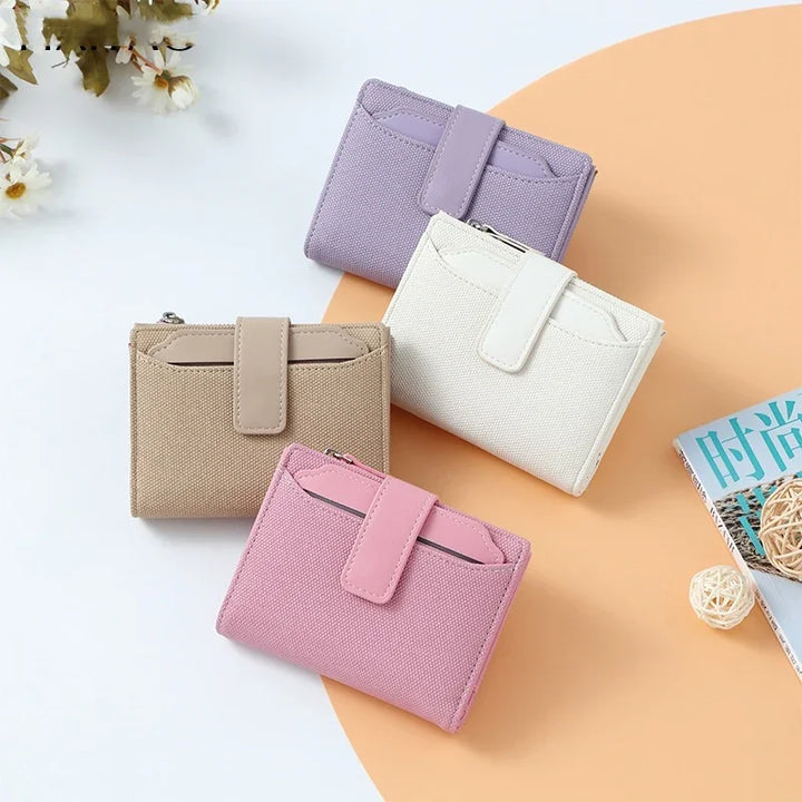 Four compact canvas wallets in beige, pink, white, and lavender on white and orange background with floral decor