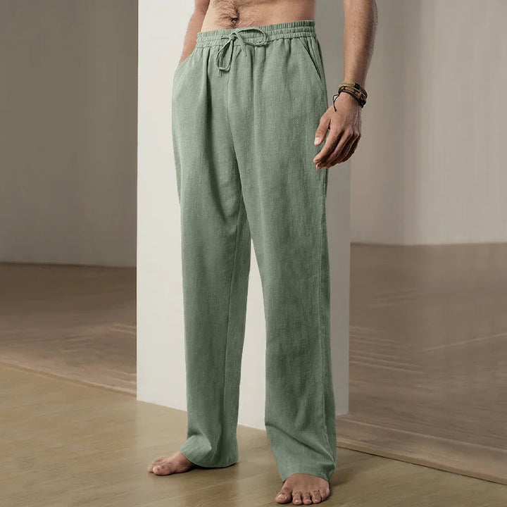Man wearing light green drawstring linen pants standing barefoot on wooden floor indoors