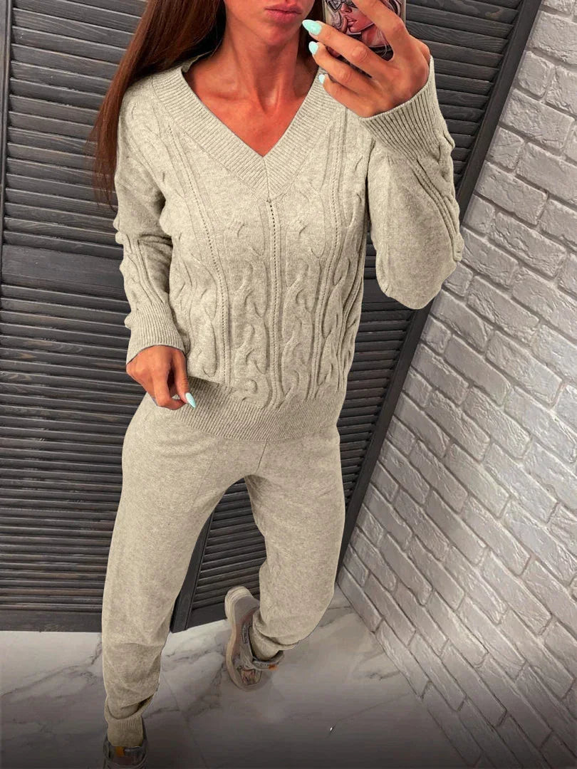 Woman wearing beige cable knit V-neck sweater and matching jogger pants posing indoors