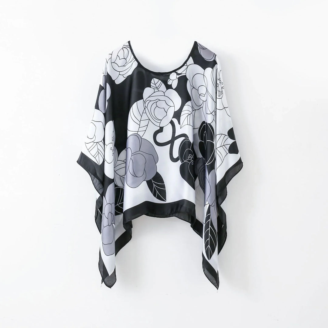 Black and white floral poncho with rose and leaf patterns hanging on white wall