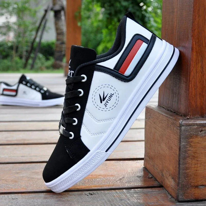 Black and white Jiyuni brand casual sneakers with red and navy detail on wooden floor outdoors