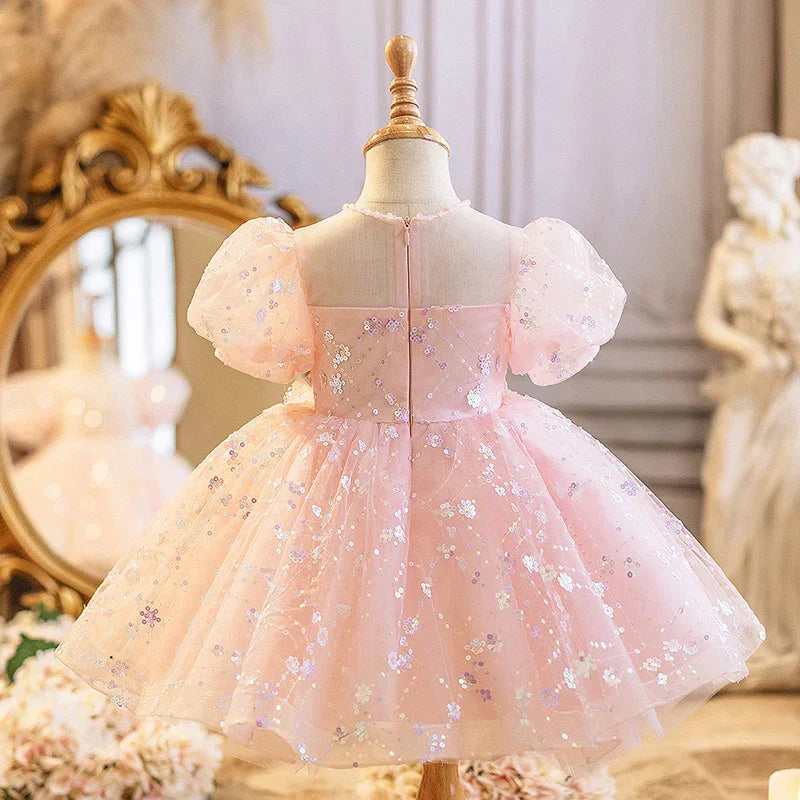 Back view of a pink toddler dress with puff sleeves and sequin floral details on a mannequin