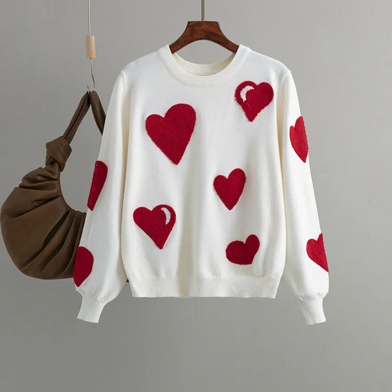 White knit sweater with red heart patterns hanging on wooden hanger against gray background