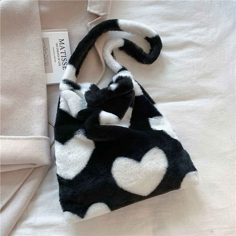Black and white faux fur handbag with heart pattern on beige fabric surface next to folded coat