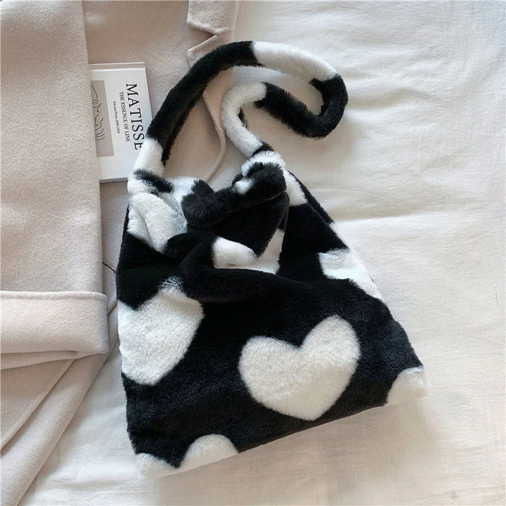 Black and white faux fur handbag with heart pattern on beige fabric surface next to folded coat