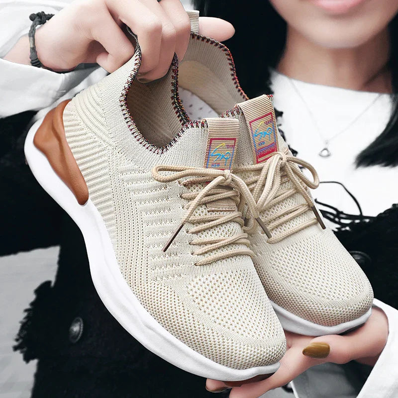 Beige knitted lightweight sneakers with laces and white sole held by person with black and white outfit