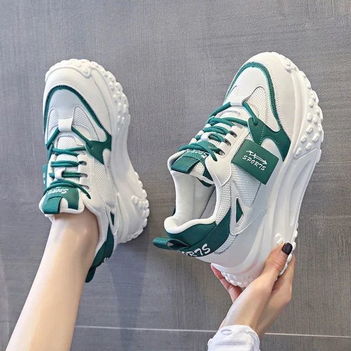 White and green chunky sports sneakers with thick textured soles worn on feet and held by hand
