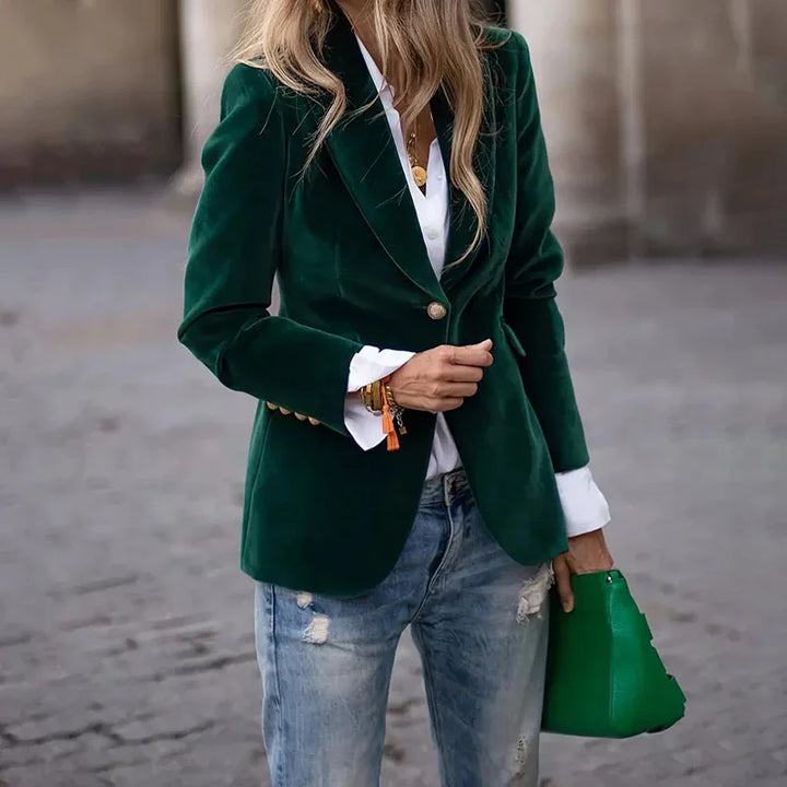 Woman wearing dark green velvet blazer with white shirt, distressed jeans, and holding a green handbag