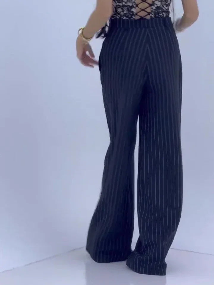 Woman wearing black pinstripe wide-leg pants and lace-up back black top on white background