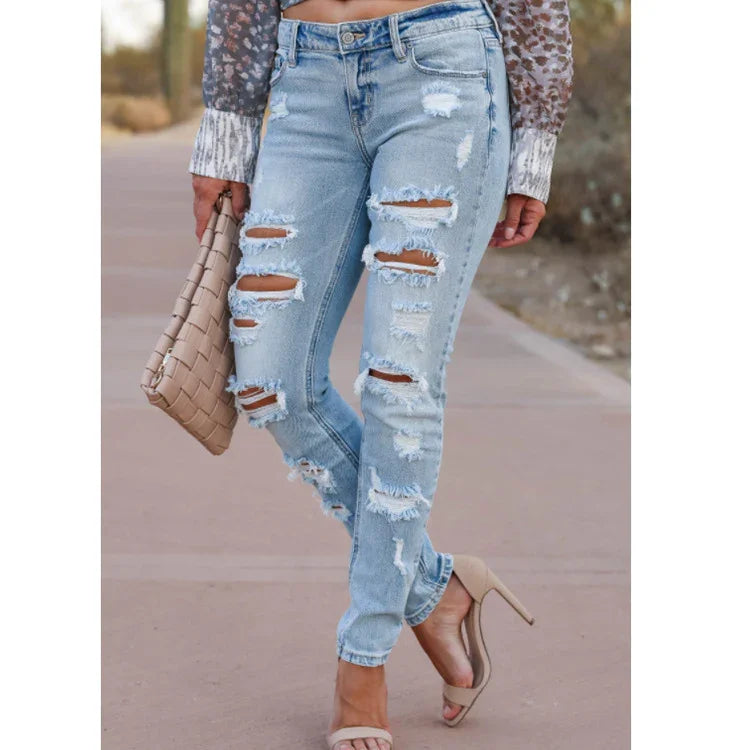 Woman wearing light blue distressed ripped jeans with nude heels and holding a woven beige clutch