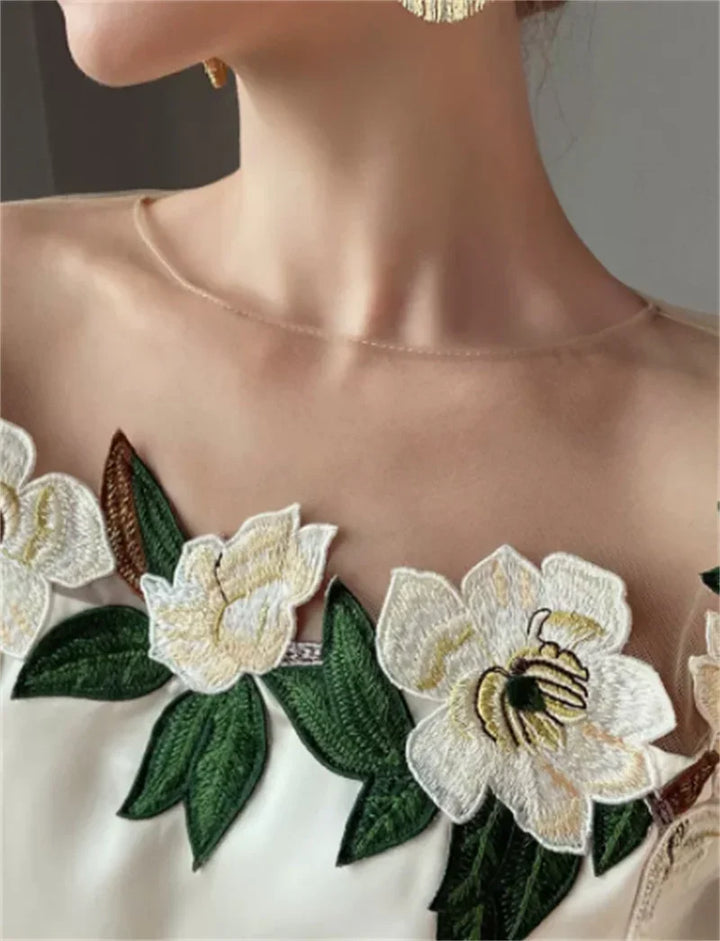Close-up of woman's neckline with floral embroidered white dress and green leaves design
