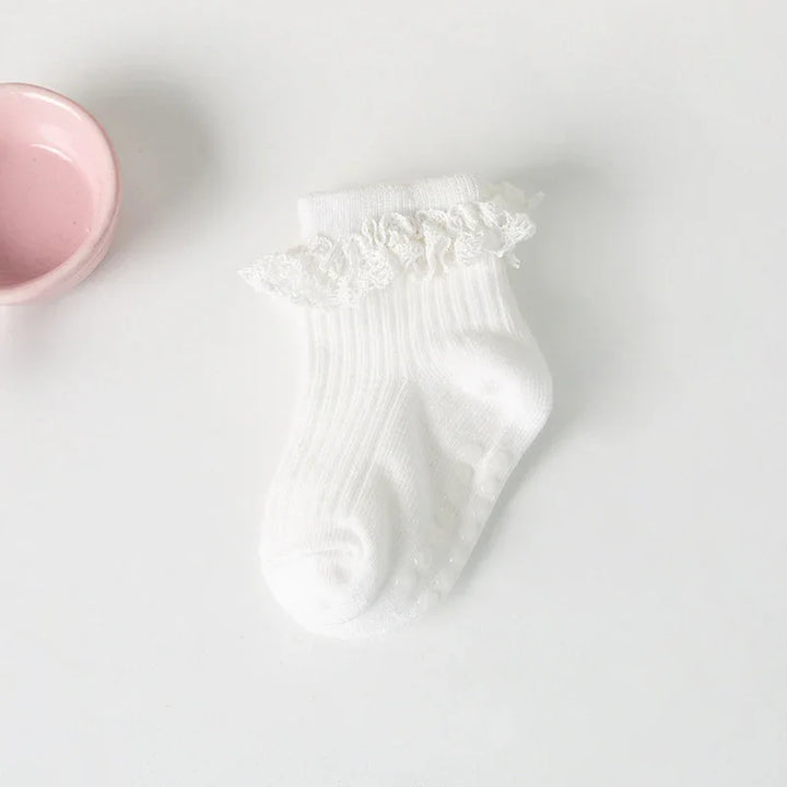 White baby socks with lace frill detail placed on white surface next to a pink ceramic bowl
