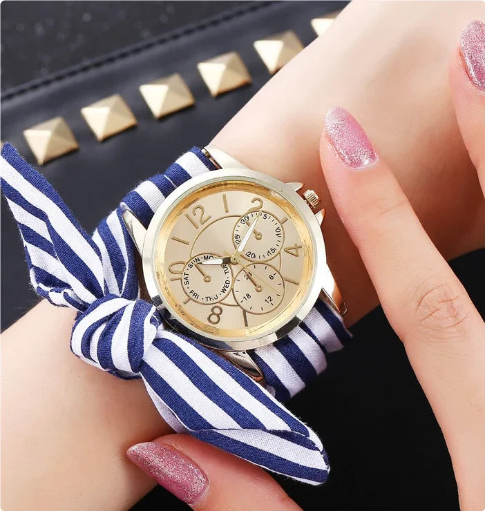 Gold wristwatch with beige face and day-date subdials on blue and white striped fabric strap tied in a bow
