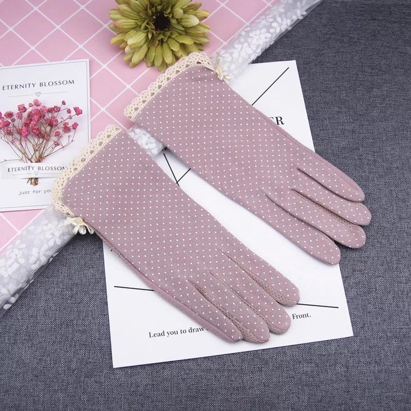 Elegant pink polka dot gloves with lace trim on gray fabric and decorative flowers