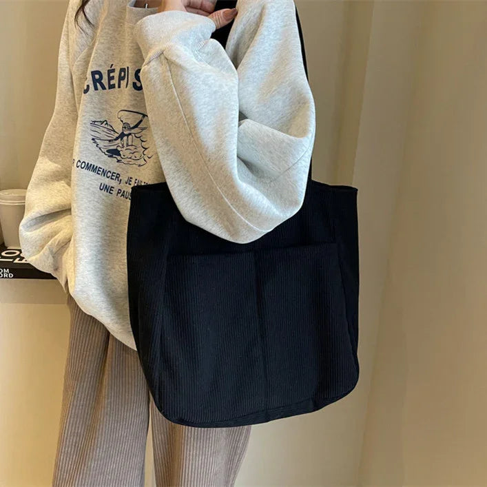 Person wearing gray graphic sweatshirt and beige corduroy pants holding black corduroy tote bag