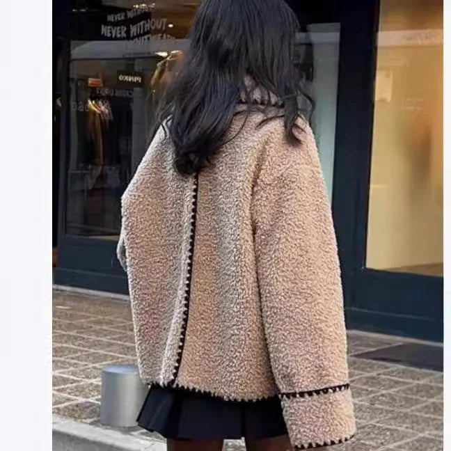 Woman wearing beige teddy coat with black trim, walking on city sidewalk near storefront