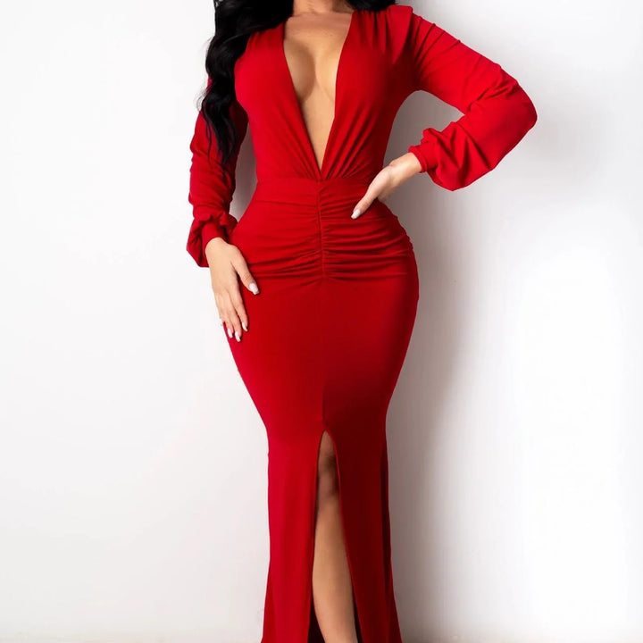 Woman in elegant red long-sleeve gown with deep neckline and front slit posing against white background