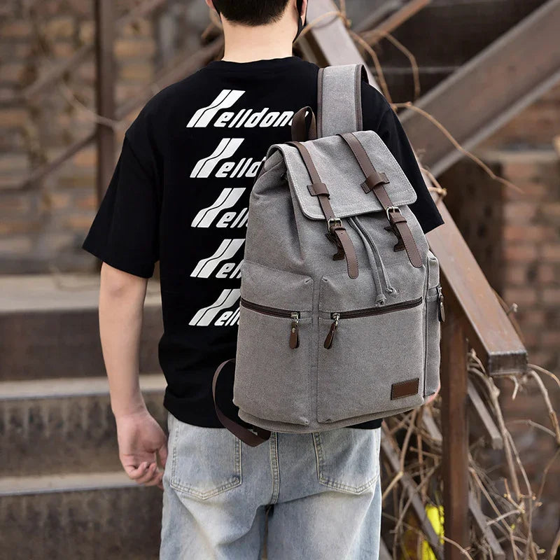 Man wearing black printed t-shirt and light jeans carrying gray canvas backpack with leather straps