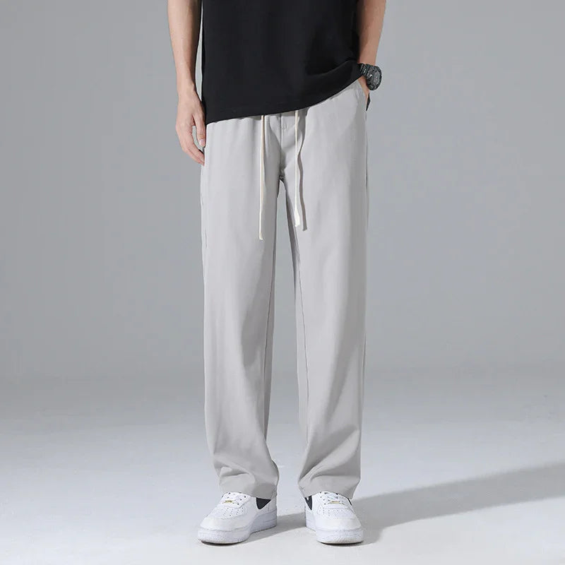 Man wearing light gray drawstring casual pants with white sneakers against gray background