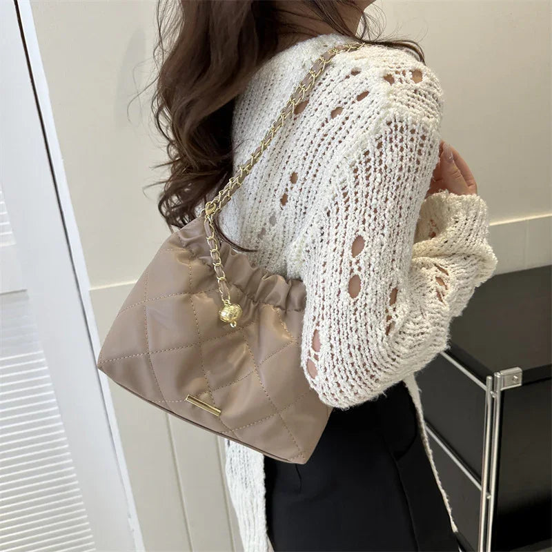 Woman wearing white knit sweater carrying beige quilted chain strap handbag indoors
