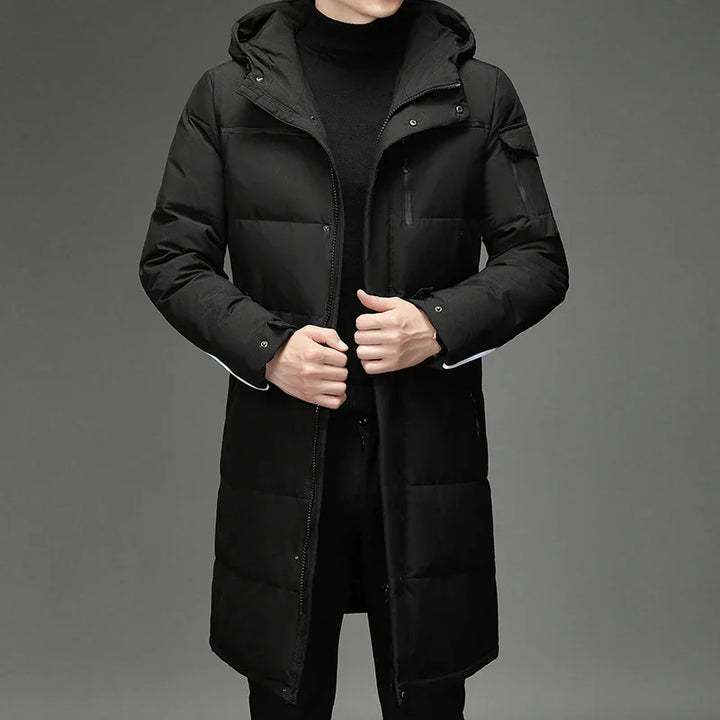 Man wearing black long puffer coat with hood and zippered pockets on gray background
