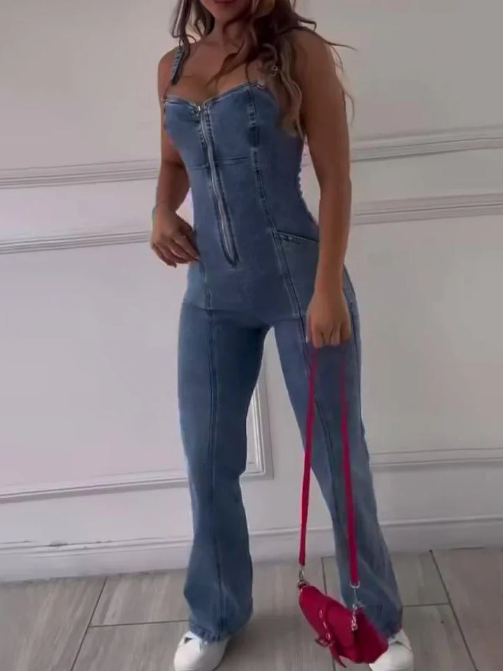 Woman wearing blue denim zip-up jumpsuit with white sneakers and holding a red handbag indoors