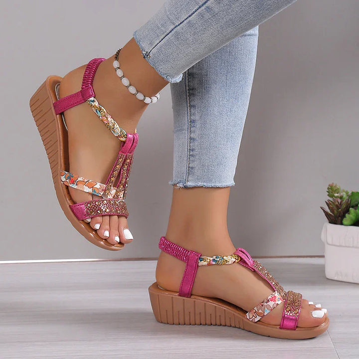 Pink wedge sandals with floral and glitter straps worn with light blue jeans and white toenail polish