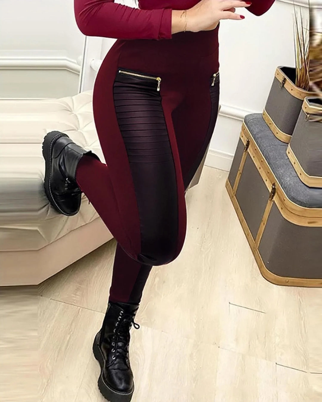Woman wearing burgundy leggings with black leather panels and zipper details paired with black combat boots indoors