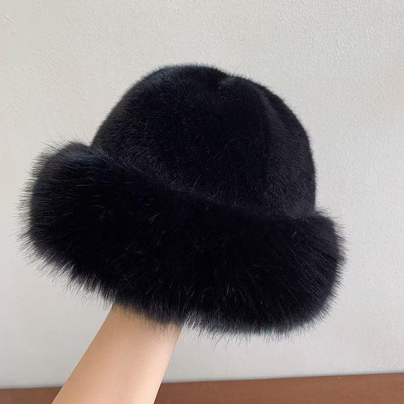 Black fuzzy winter hat with a soft thick fur brim held against a white wall background