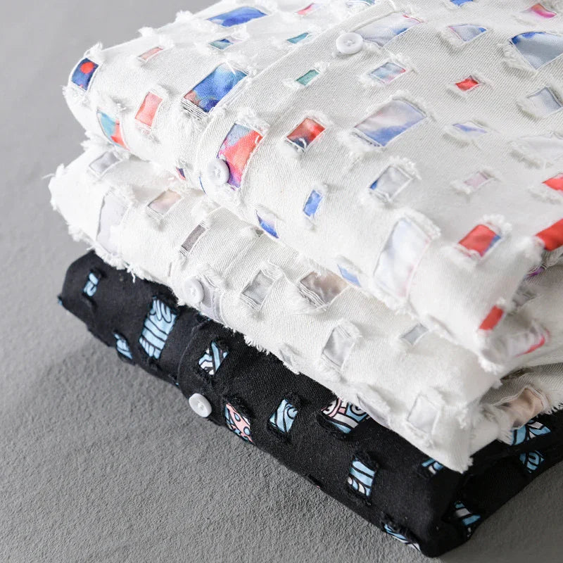 Stack of folded white and black shirts with cut-out square patterns revealing colorful fabric underneath