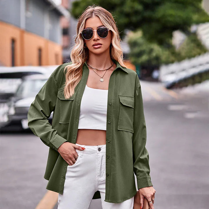 Blonde woman wearing olive green button-up shirt, white crop top, white pants, and sunglasses in urban street