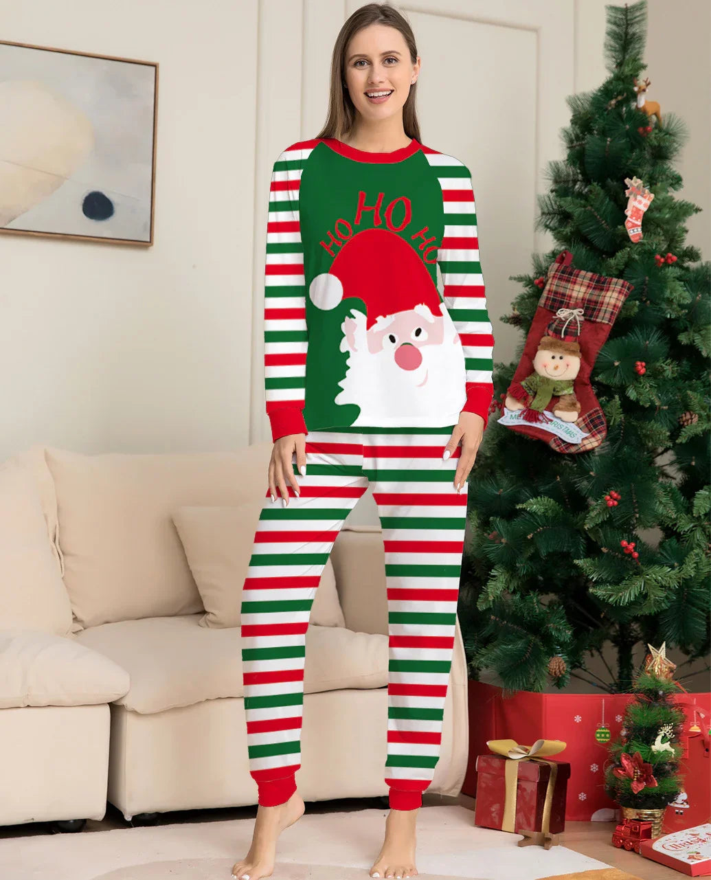 Woman in Christmas pajamas with Santa and Ho Ho Ho text standing by decorated Christmas tree and gifts