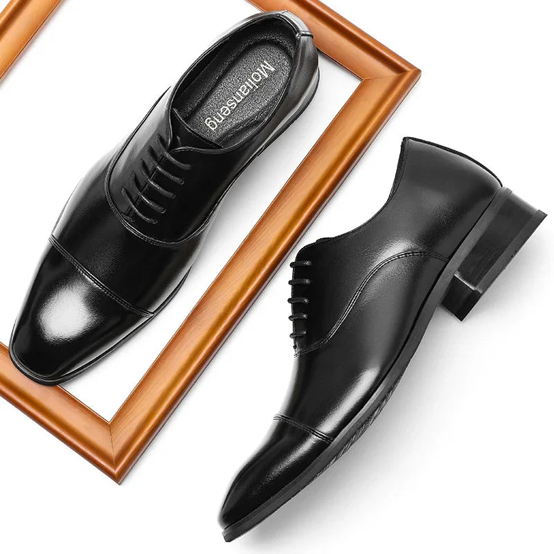 Pair of polished black leather men's dress shoes on white background with wooden frame