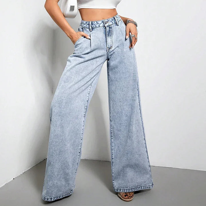 Woman wearing high-waisted wide-leg light blue denim jeans and white crop top against white wall